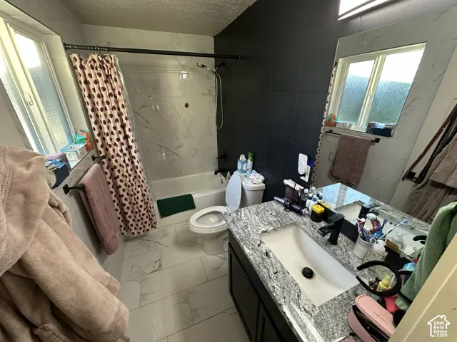 Bathroom featuring large-format tile flooring, vanity with stone-patterned countertop, under-mount sink with matte black hardware, and floor-to-ceiling tile shower surround