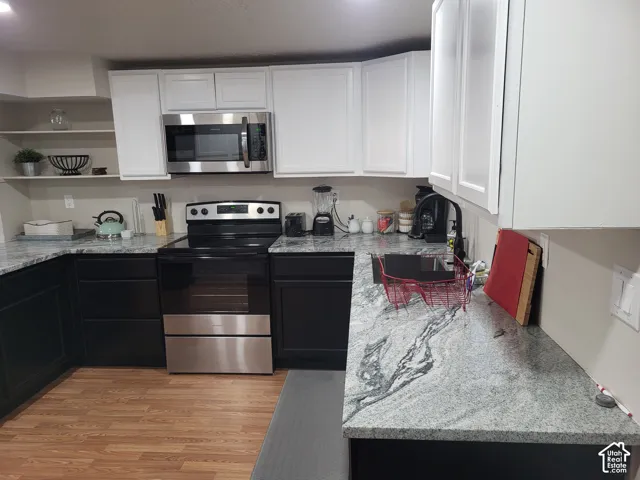 Kitchen featuring two-tone cabinetry, stone-finish countertops, stainless steel appliances, open shelving, and wood-finish flooring