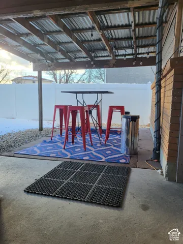 Covered patio featuring a concrete floor, corrugated metal roof, exposed timber beams, and a brick exterior wall