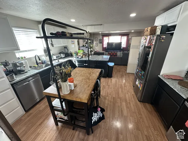 Kitchen featuring wood-finish flooring, stone-surfaced countertops, black lower cabinetry, white upper cabinetry, and stainless steel dishwasher