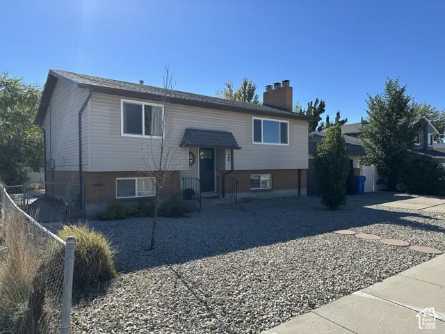 Split-level exterior featuring brick and horizontal siding, a prominent brick chimney, an arched metal door awning, and gravel landscaping