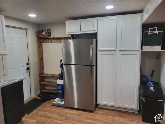 Stainless steel refrigerator, custom white shaker-style cabinetry, wood-finish flooring, and recessed ceiling lighting