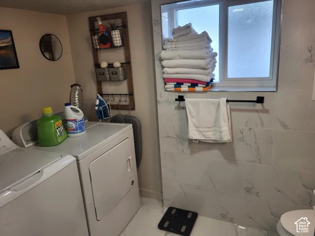 Laundry room featuring large-format tile flooring, wall-mounted matte black towel hardware, and natural stone-finish wall tile surrounding a window