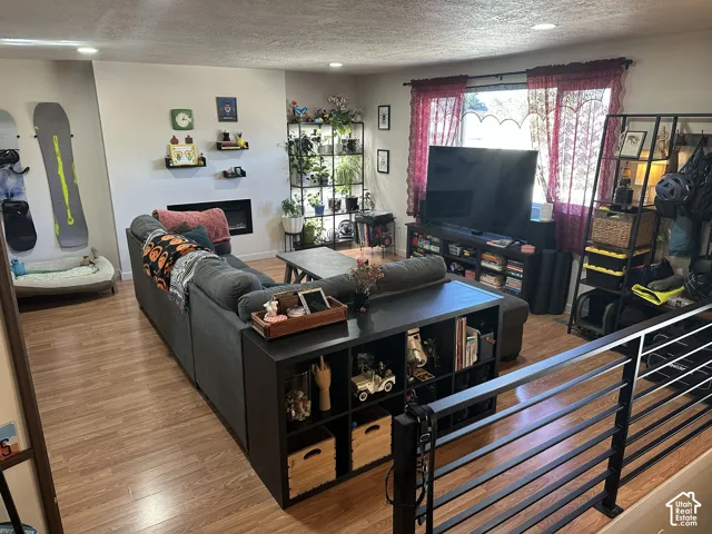 Living area featuring wood-finish flooring, recessed lighting, and a linear wall-mounted fireplace with black metal stair railing