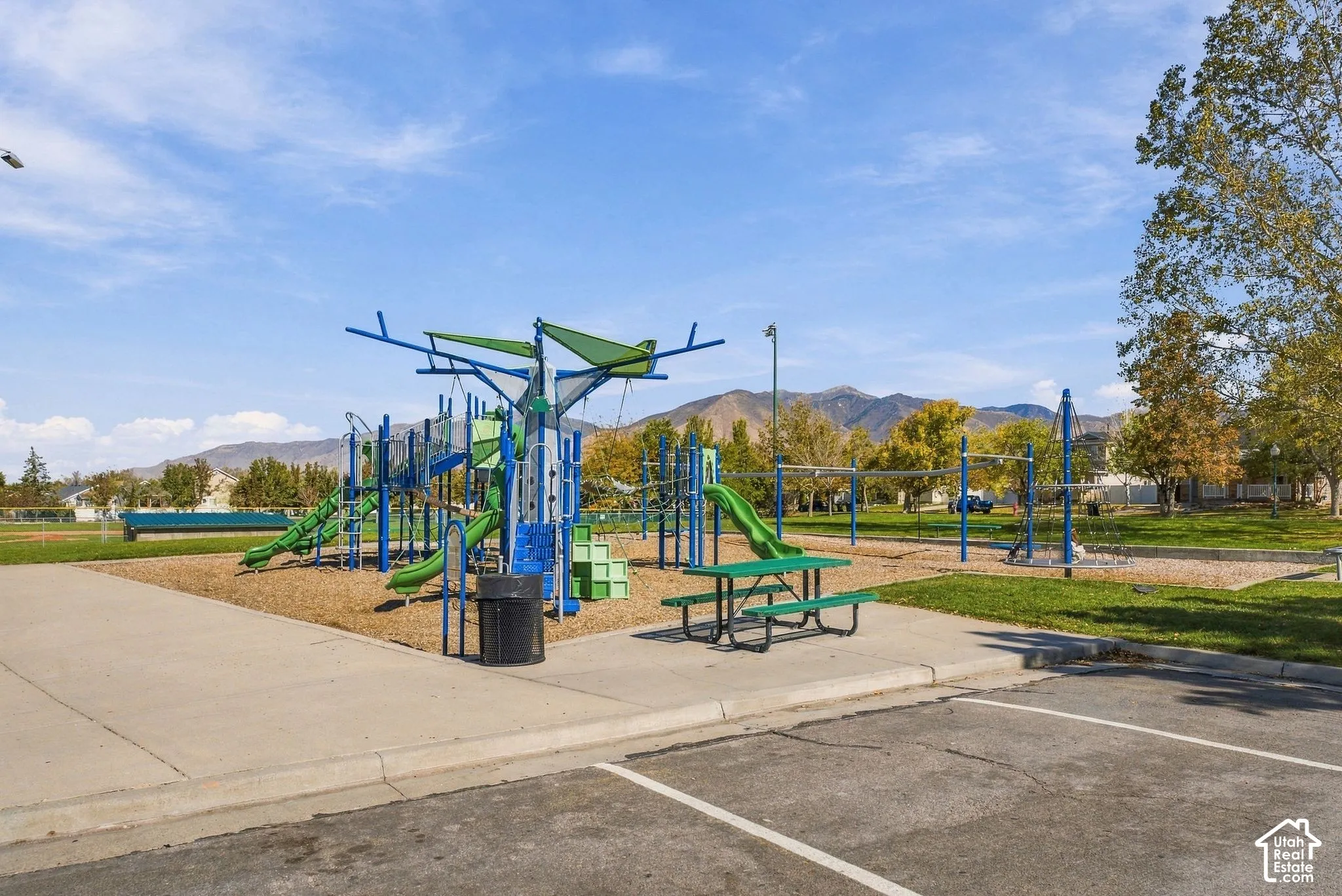 Community recreation area featuring a multi-component playground structure, integrated picnic seating, concrete paving, and a mountain backdrop
