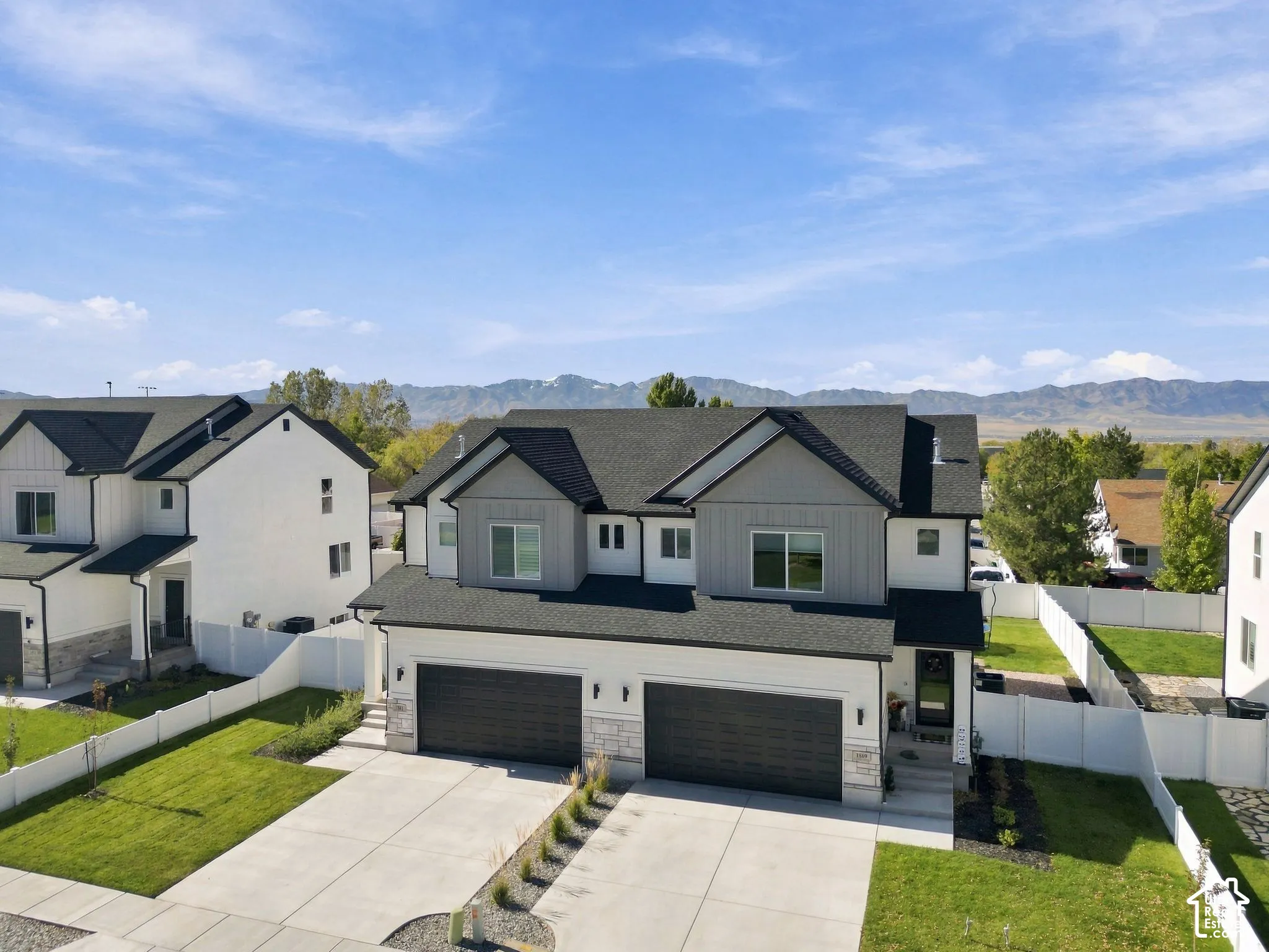 Two-story exterior featuring a mixed material facade of light-toned siding and stone accents, a dual-bay garage, dark roofing, and a mountain backdrop