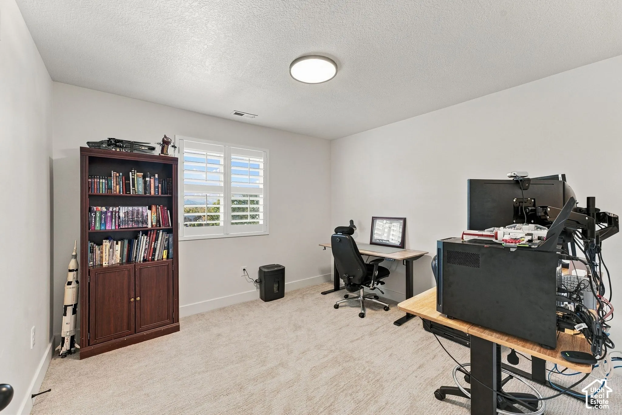 Room featuring neutral-toned carpeting, crisp wall finishes, a flush-mount ceiling light, and plantation shutters