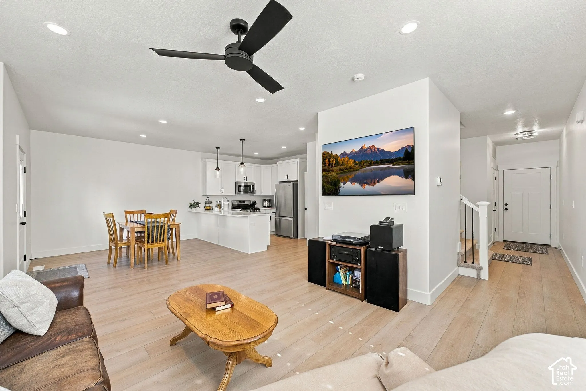 Open-concept interior featuring wood-finish flooring, recessed lighting, a modern matte black ceiling fan, and white cabinetry with stainless steel appliances