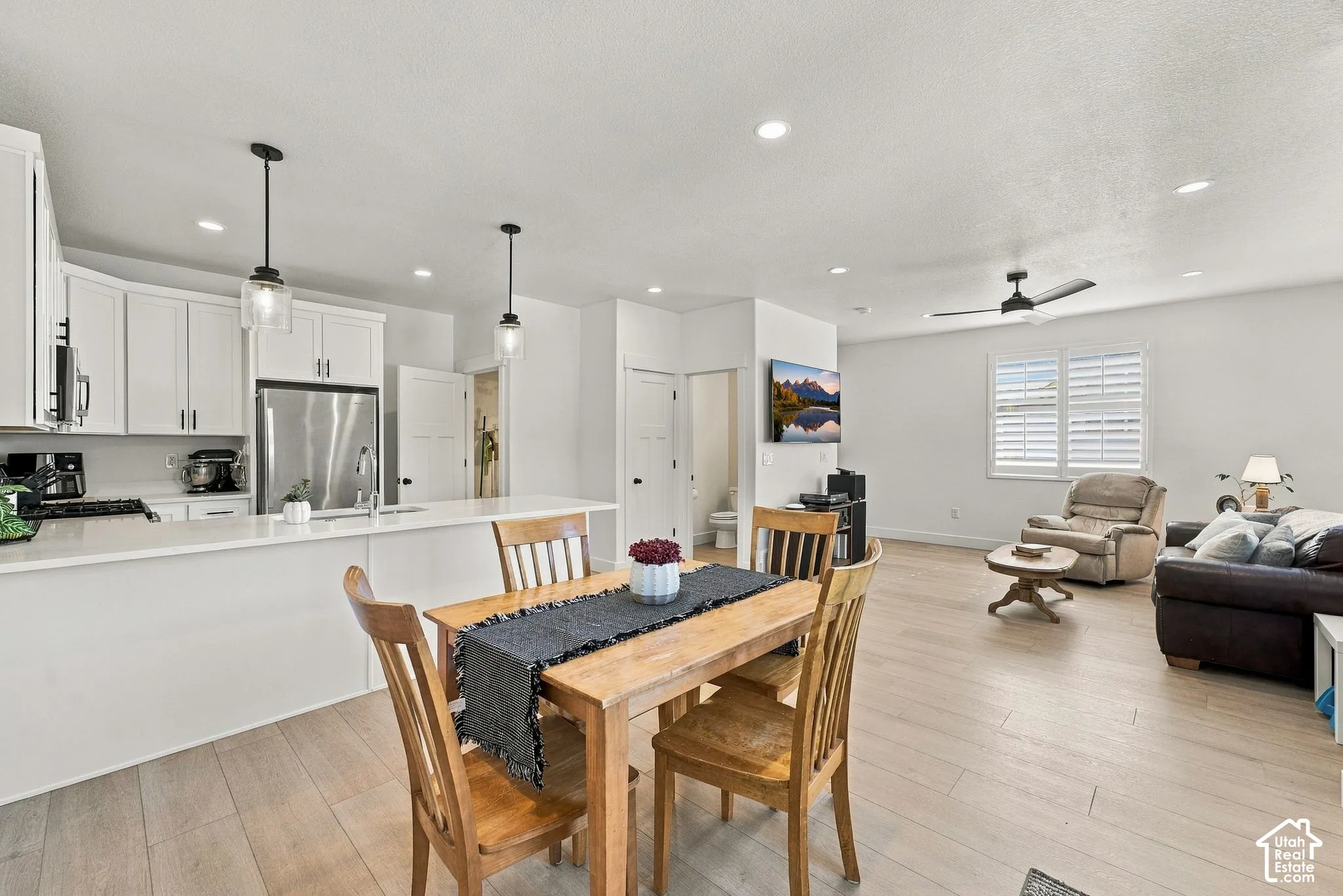 Open-concept living space featuring wood-finish flooring, white shaker-style cabinetry, a quartz kitchen island, recessed lighting, and suspended pendant fixtures