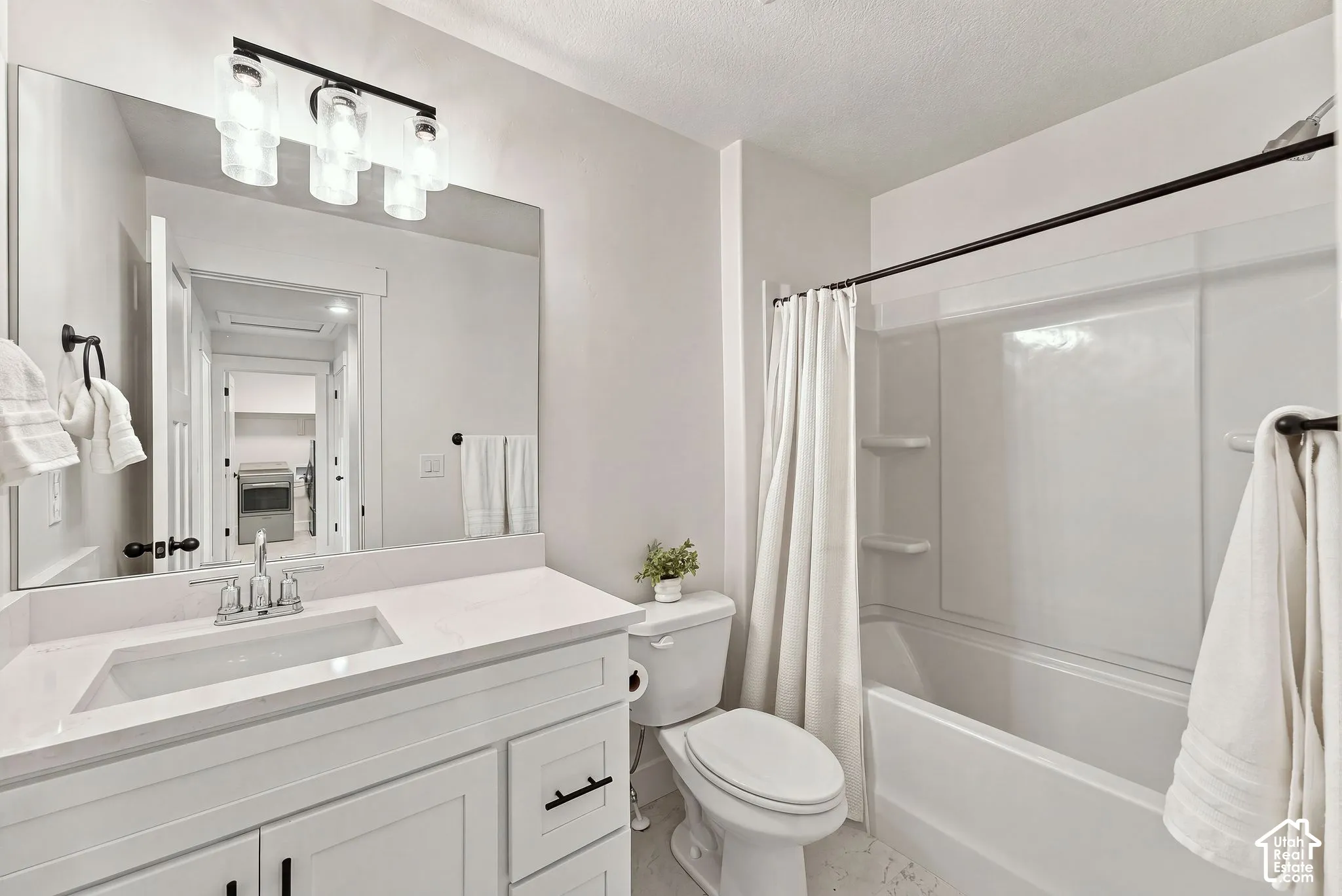 Bathroom featuring a white vanity with a rectangular sink, stone-finish countertop, three-light vanity fixture, and a shower-tub combination with a white surround