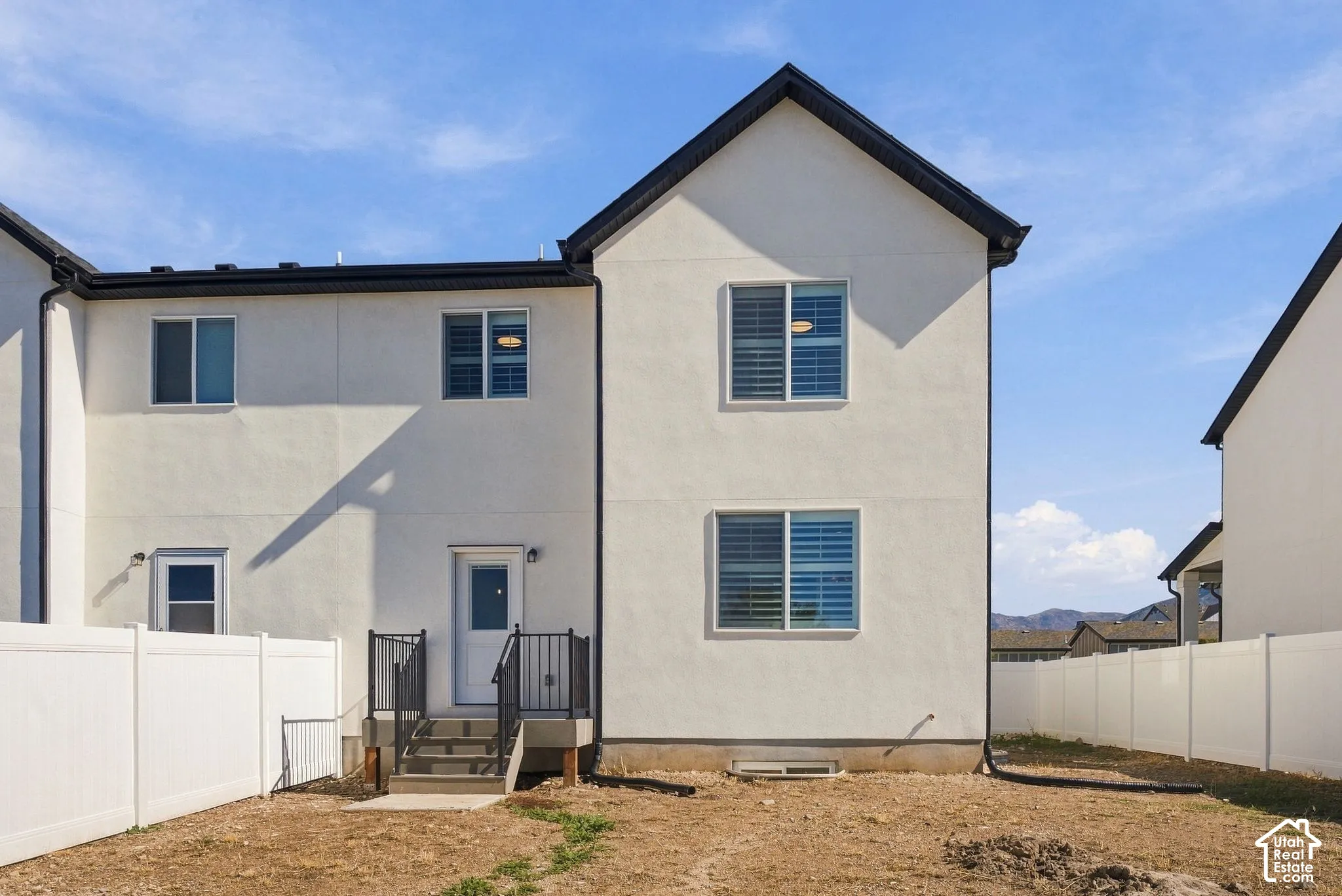 Stucco exterior with a gabled roofline, featuring a private rear entry with metal railing and stairs, sliding windows, and a surrounding white vinyl privacy fence