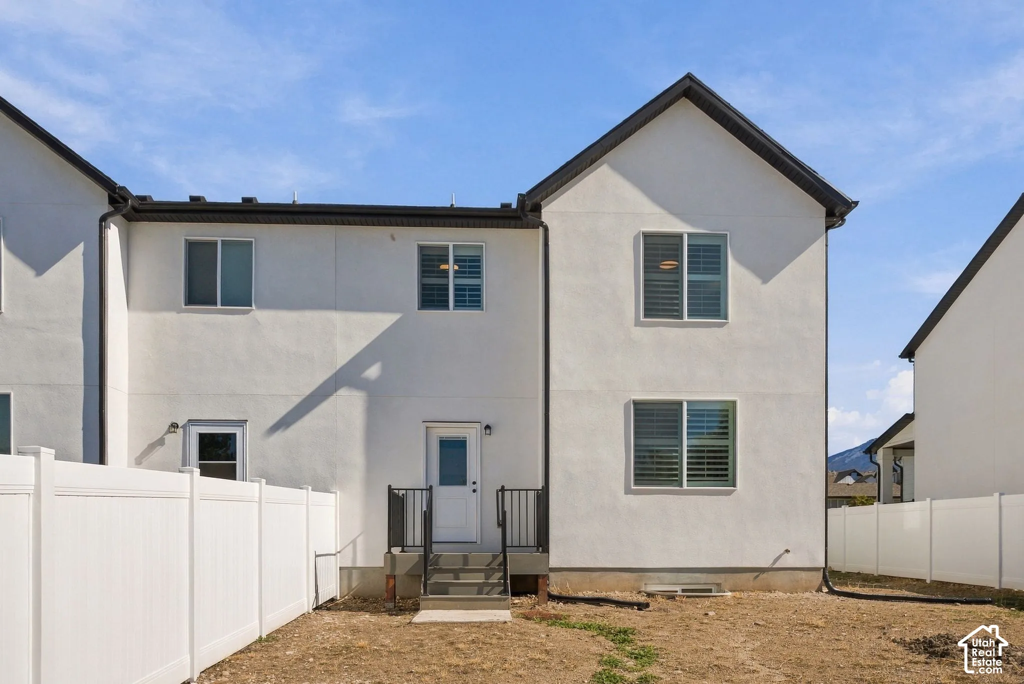 Two-story exterior featuring light-toned stucco siding, dark-trimmed gabled rooflines, double-pane windows, and a private fenced outdoor area with a concrete porch entry