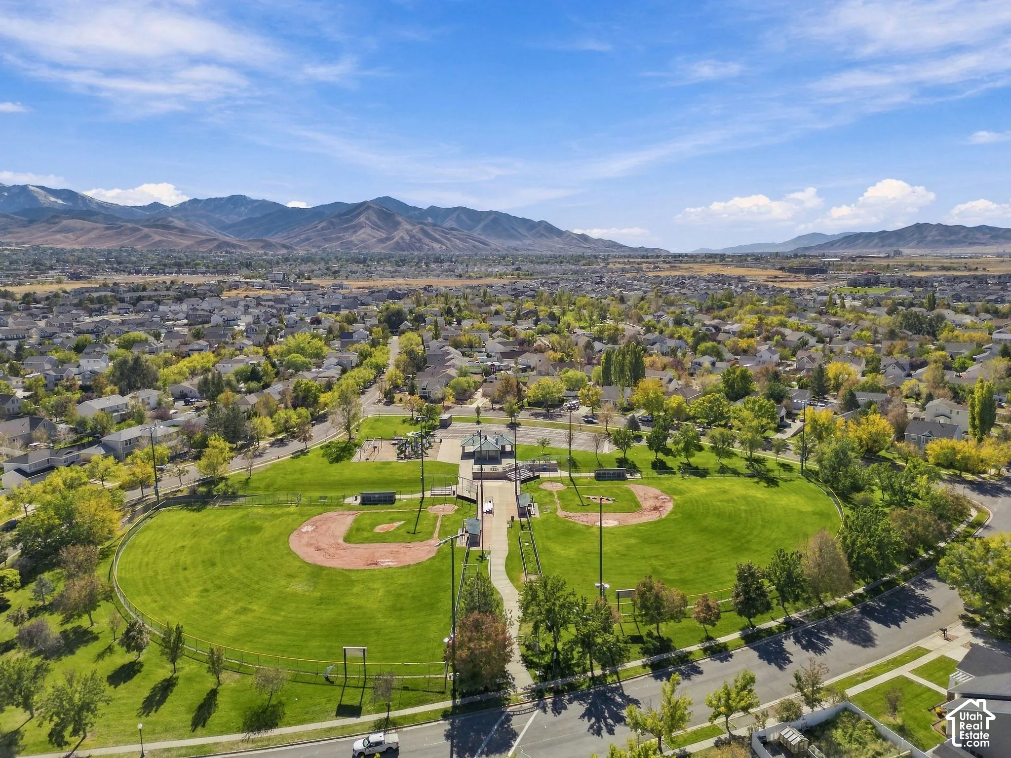 Aerial perspective of a park featuring manicured lawns, baseball diamonds, mature trees, and a mountain range backdrop