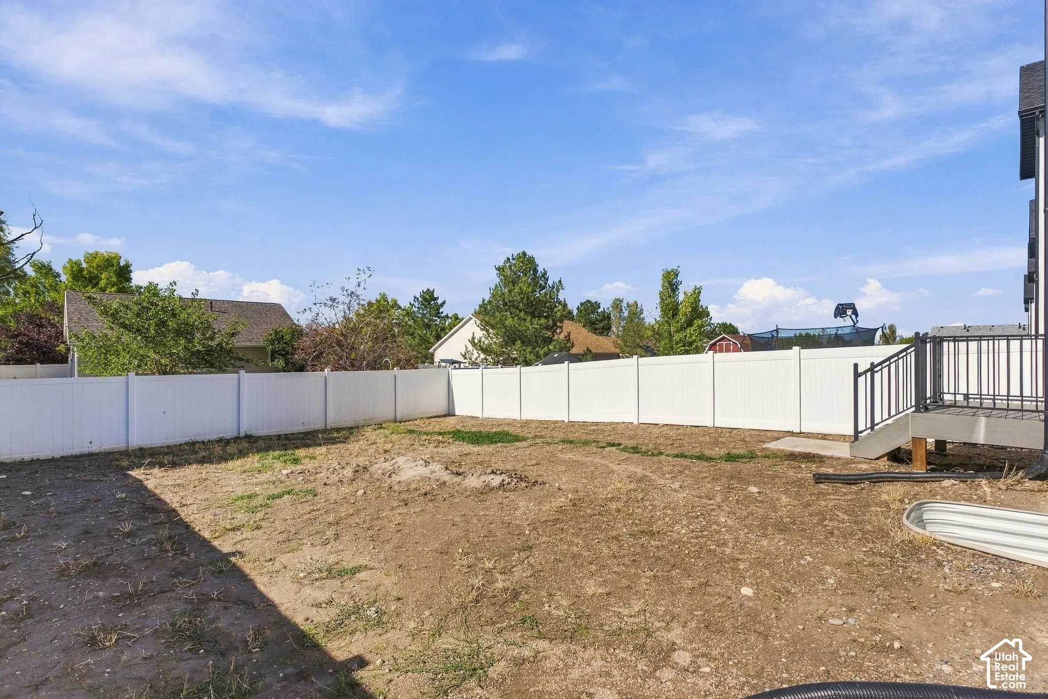 Backyard area featuring a white vinyl privacy fence, elevated rear deck with black metal railing, and a corrugated metal basin