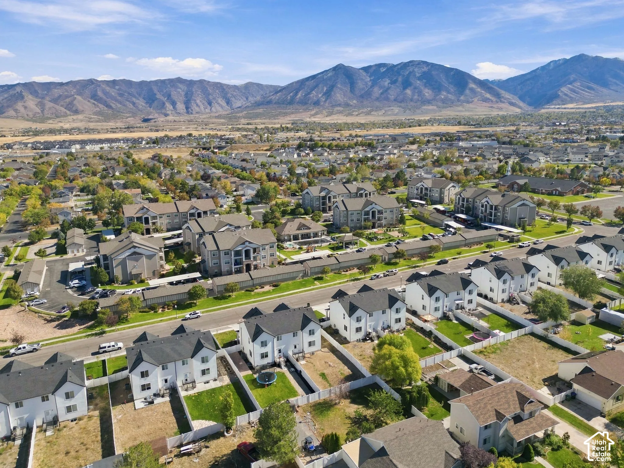 Aerial perspective of a suburban neighborhood featuring multi-level residential structures, fenced private rear yards, and a backdrop of mountain scenery