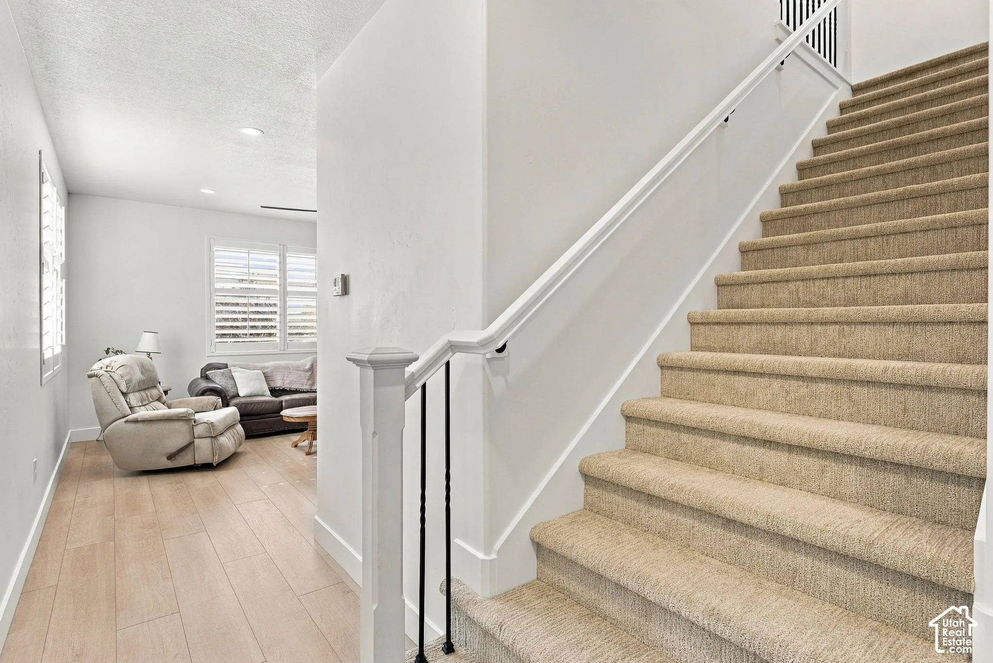 Staircase featuring carpeted treads, a white handrail, and wrought-iron balusters, complemented by wood-finish flooring and shuttered windows