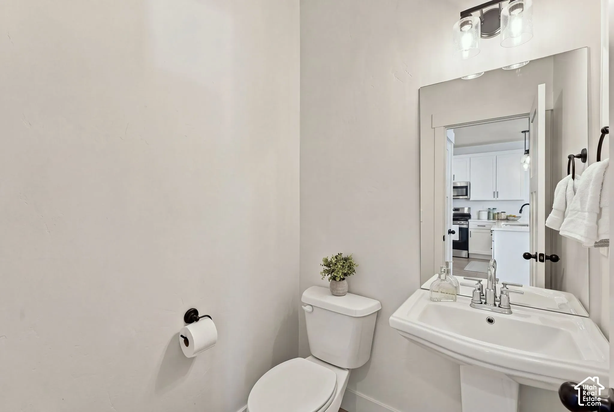 Powder room featuring a wall-mounted pedestal sink, matte black hardware, frameless mirror, and dual-light vanity fixture