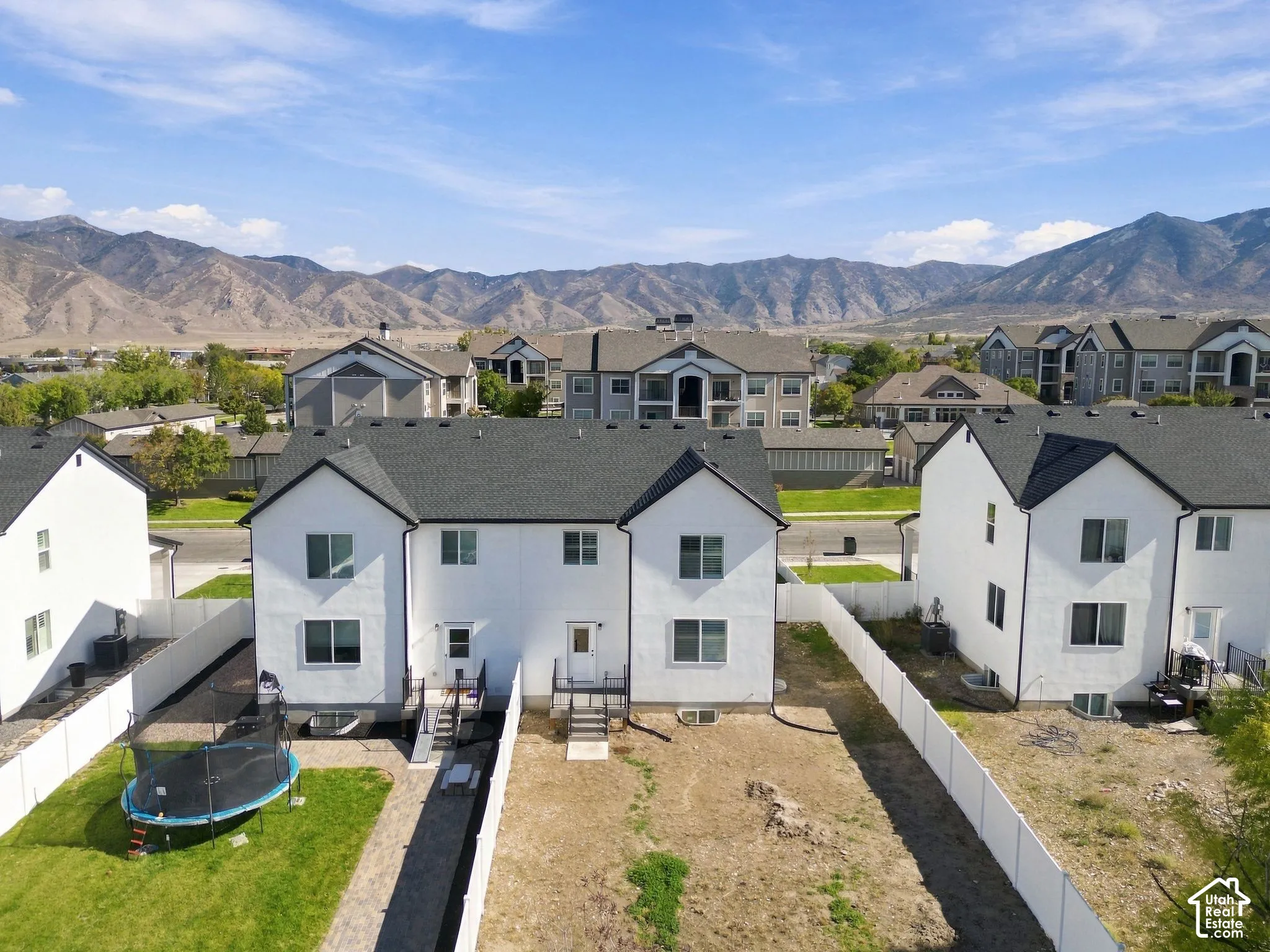 Aerial perspective featuring white stucco exterior buildings with dark shingle roofing, enclosed rear yards, and mountain backdrop