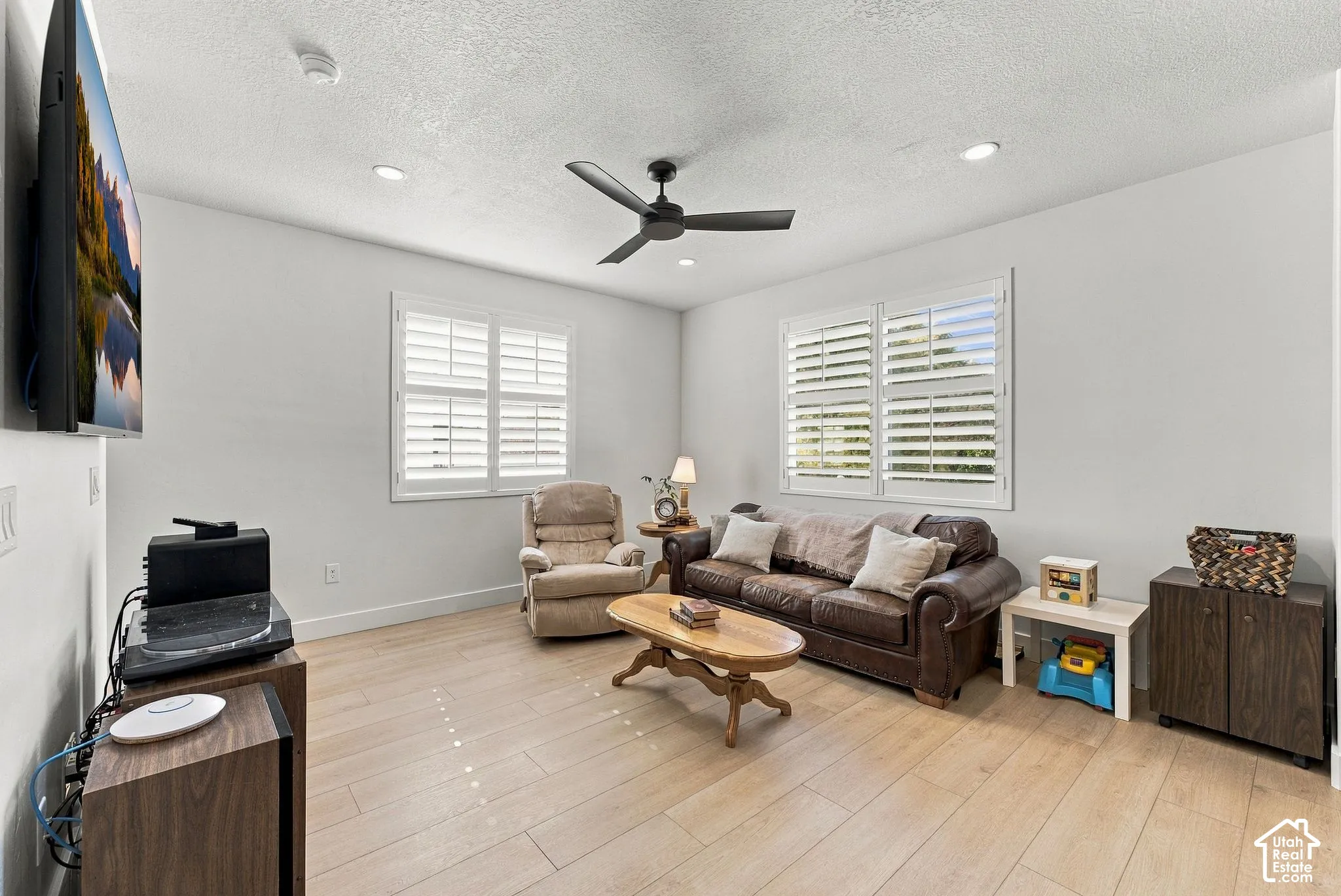 Living area featuring wood-finish flooring, recessed lighting, a matte black ceiling fan, and plantation shutters