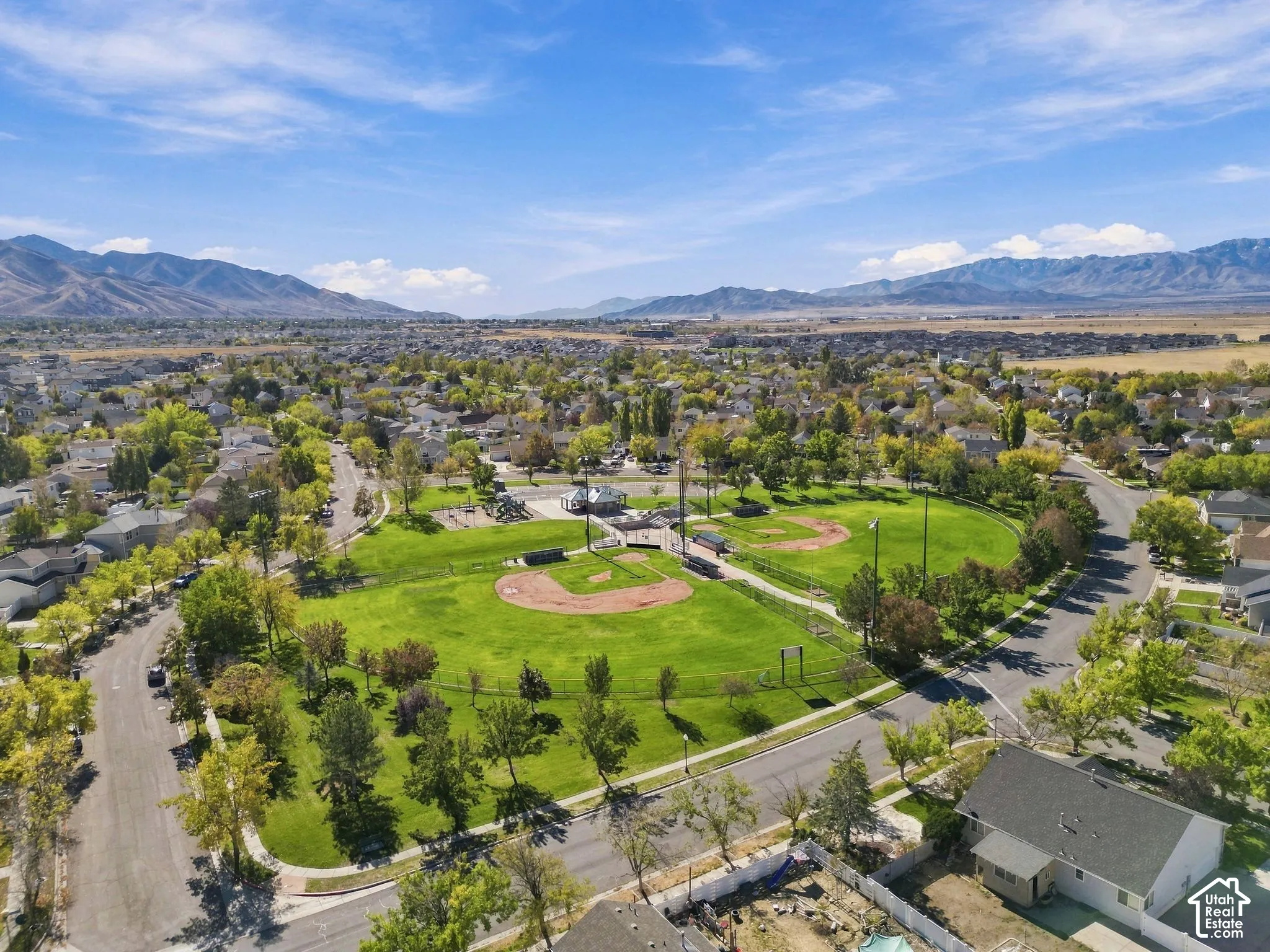 Aerial perspective featuring a public park with baseball diamonds, open green space, and mature trees, set against a mountain backdrop