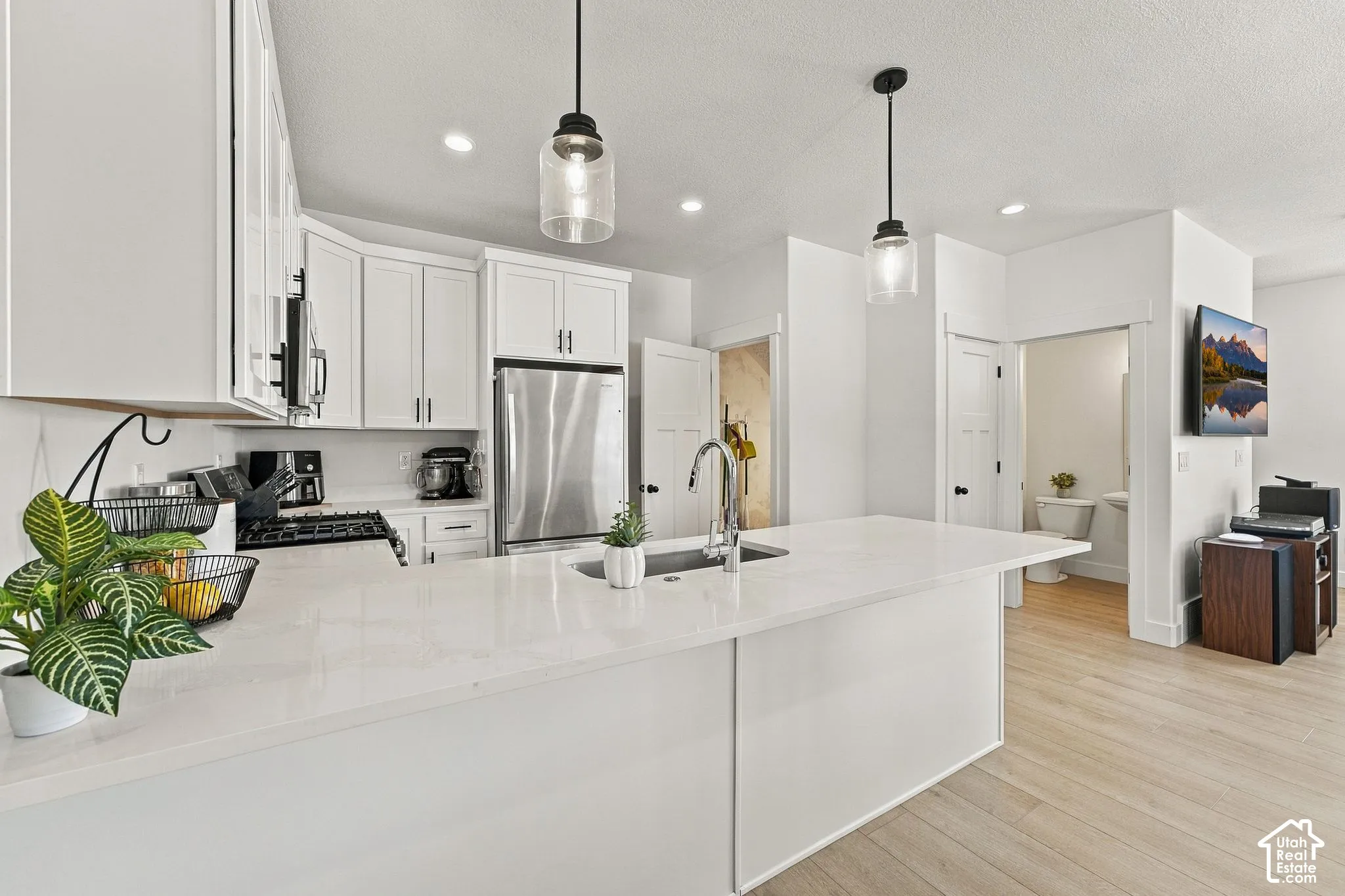Kitchen featuring a white quartz island with an integrated stainless steel sink, cabinetry with clean-lined shaker-style doors, wood-finish flooring, and glass pendant lighting