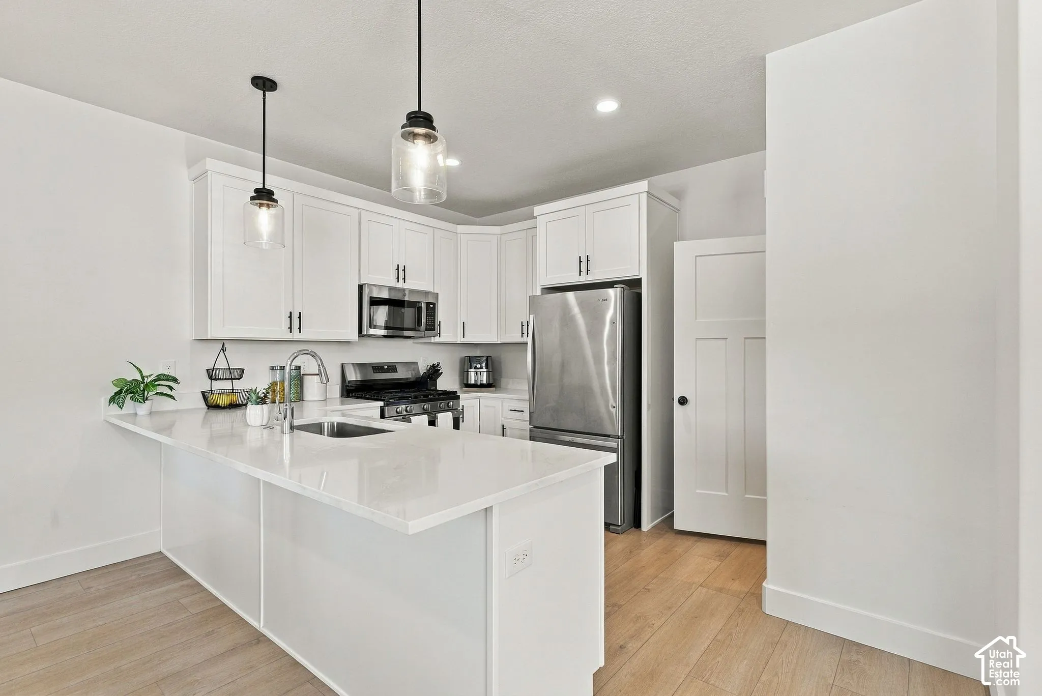 Kitchen featuring white shaker-style cabinetry, a quartz countertop island, stainless steel appliances, pendant lighting, and wood-finish flooring