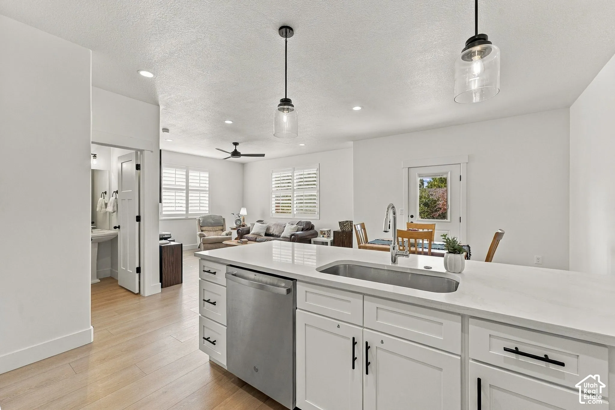 Kitchen island with solid surface countertop, stainless steel undermount sink, white shaker-style cabinetry, matte black hardware, and wood-finish flooring