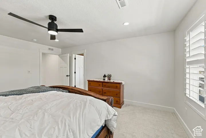 Neutral interior featuring light-toned carpeting, white window shutters, a matte black ceiling fan, and recessed lighting