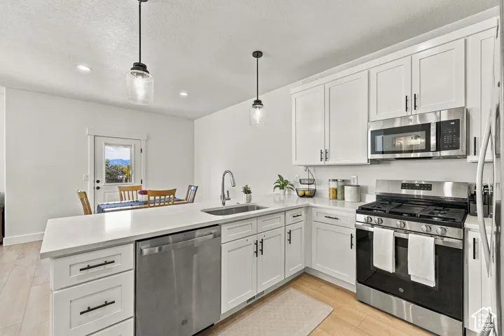 Kitchen featuring white shaker-style cabinetry, quartz countertops, stainless steel appliances, dual pendant lighting, and wood-finish flooring