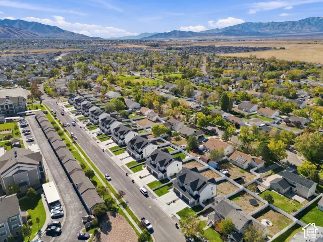 Aerial perspective of suburban residential neighborhood featuring asphalt roadways, single-family dwellings with pitched rooflines, mature deciduous trees, and a mountain range backdrop
