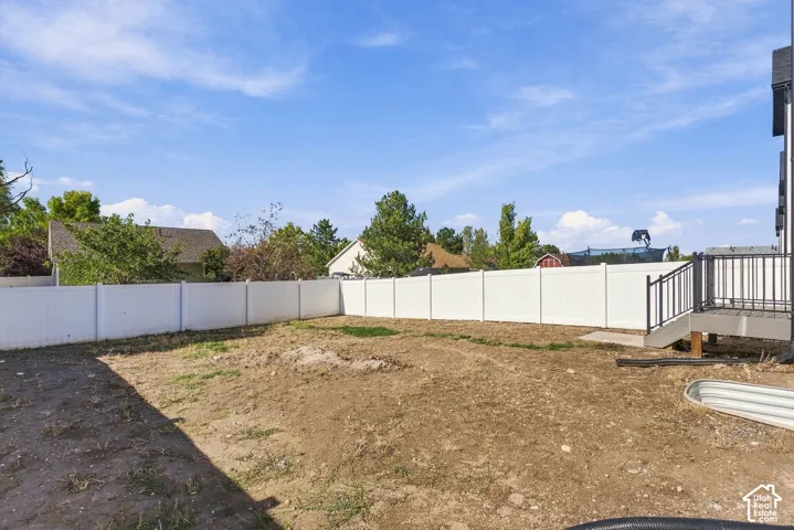 Backyard area featuring a white vinyl privacy fence, elevated rear deck with black metal railing, and a corrugated metal basin