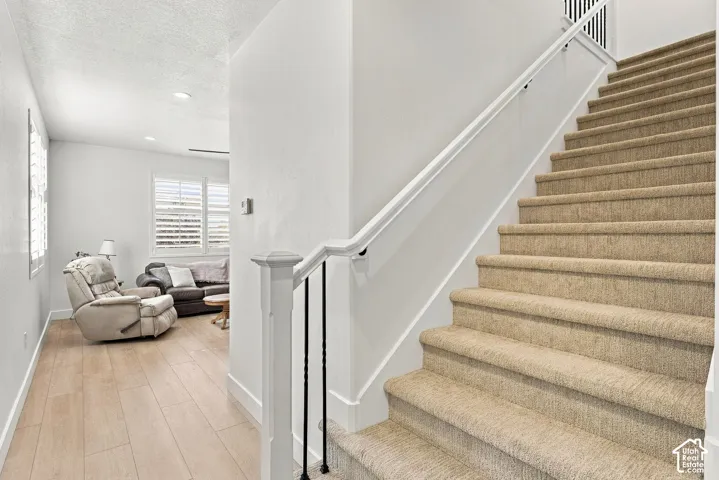 Staircase featuring carpeted treads, a white handrail, and wrought-iron balusters, complemented by wood-finish flooring and shuttered windows