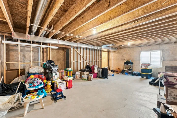 Unfinished basement featuring exposed wood joist ceilings, concrete flooring, perimeter concrete walls, and a recessed window
