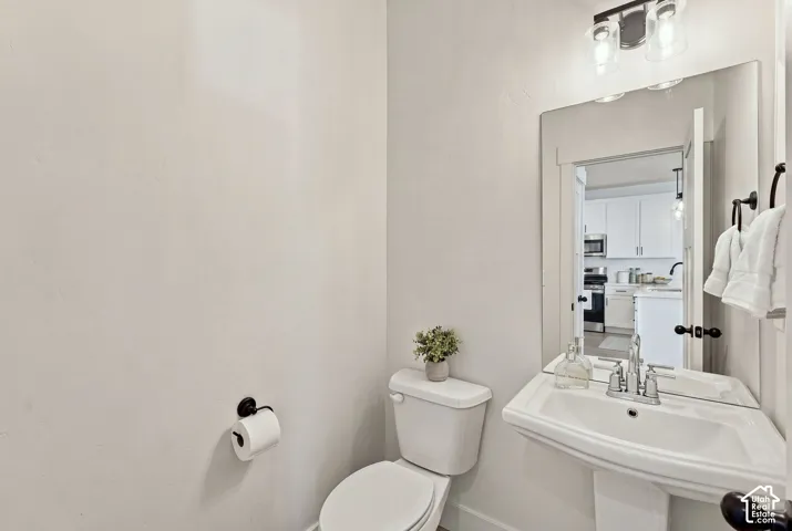 Powder room featuring a wall-mounted pedestal sink, matte black hardware, frameless mirror, and dual-light vanity fixture