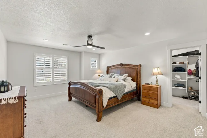 Neutral-toned carpeted interior featuring a matte black ceiling fan, recessed lighting, plantation shutters, and a built-in closet with integrated shelving