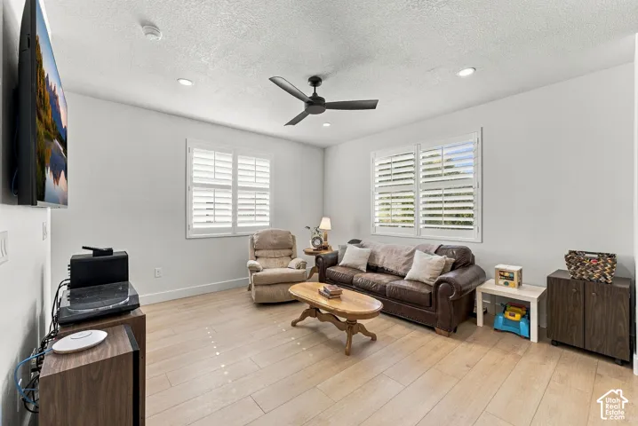Living area featuring wood-finish flooring, recessed lighting, a matte black ceiling fan, and plantation shutters