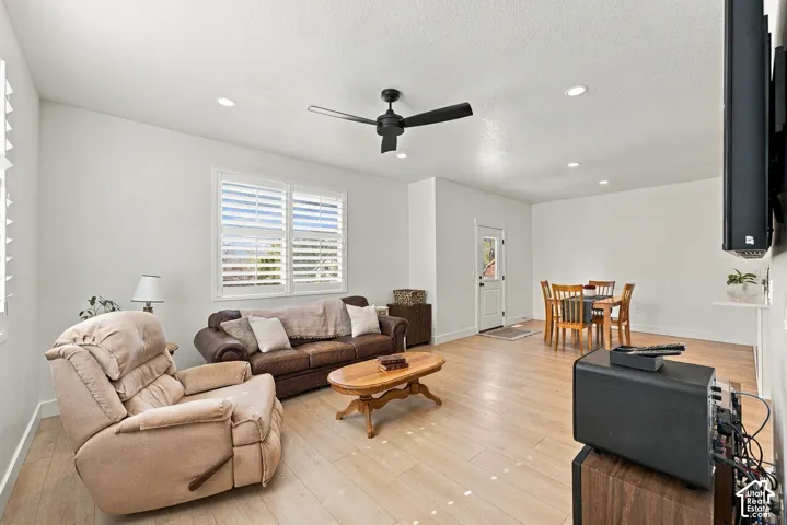 Open-concept interior featuring light wood-finish flooring, recessed lighting, a matte black ceiling fan, and plantation shutters