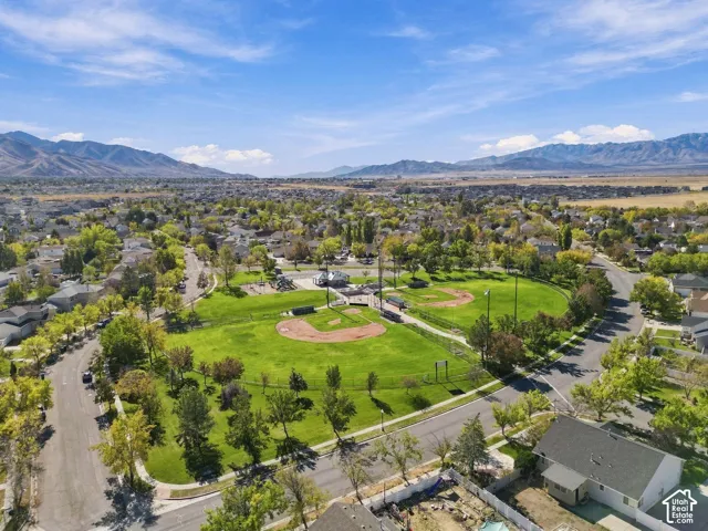 Aerial perspective featuring a public park with baseball diamonds, open green space, and mature trees, set against a mountain backdrop