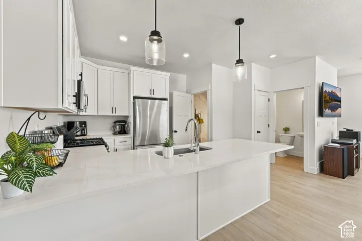 Kitchen featuring a white quartz island with an integrated stainless steel sink, cabinetry with clean-lined shaker-style doors, wood-finish flooring, and glass pendant lighting