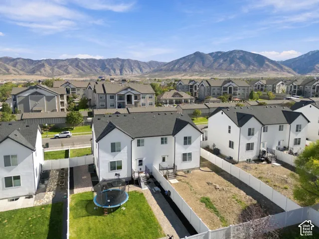 Aerial exterior featuring two-story residential structures with white stucco siding, dark shingled roofs, enclosed vinyl fencing, and mountain terrain backdrop
