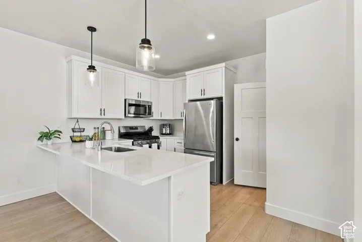Kitchen featuring white shaker-style cabinetry, a quartz countertop island, stainless steel appliances, pendant lighting, and wood-finish flooring