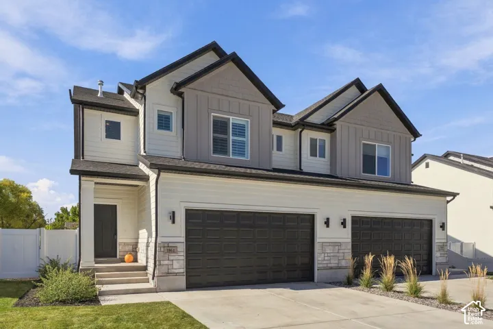 Multi-story residence featuring a combination of horizontal lap siding and vertical board-and-batten accents, two-car garage with carriage-style doors, stone veneer foundation cladding, and peaked roof gables