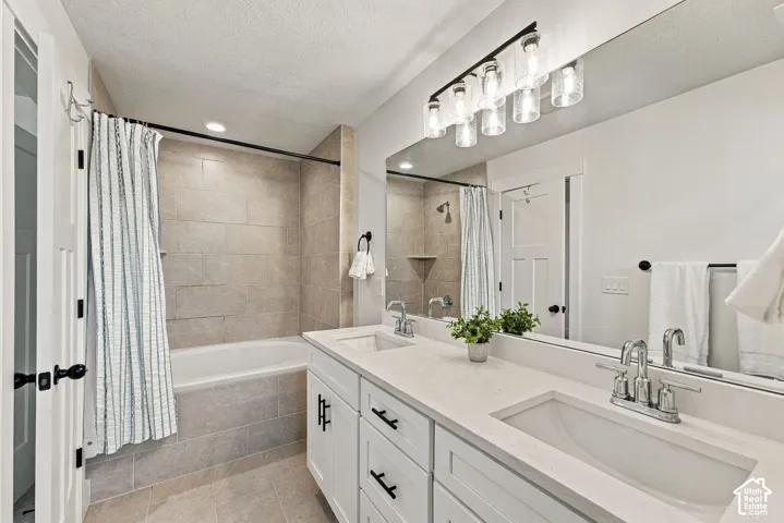 Double vanity with white cabinetry, light-toned stone-finish countertops, dual integrated sinks, and matte black hardware, featuring a full-width wall mirror, five-light glass fixture, and a tiled tub and shower combination