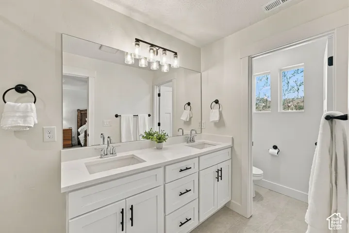 Dual vanity featuring white cabinetry, stone-finish countertops, undermount sinks, and matte black hardware, accented by a full-width mirror and a multi-bulb light fixture
