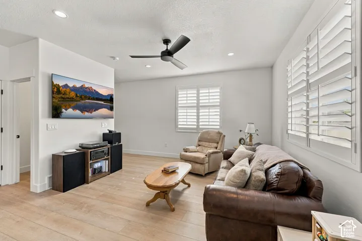 Living area featuring light wood-finish flooring, recessed lighting, matte black ceiling fan, and plantation shutters