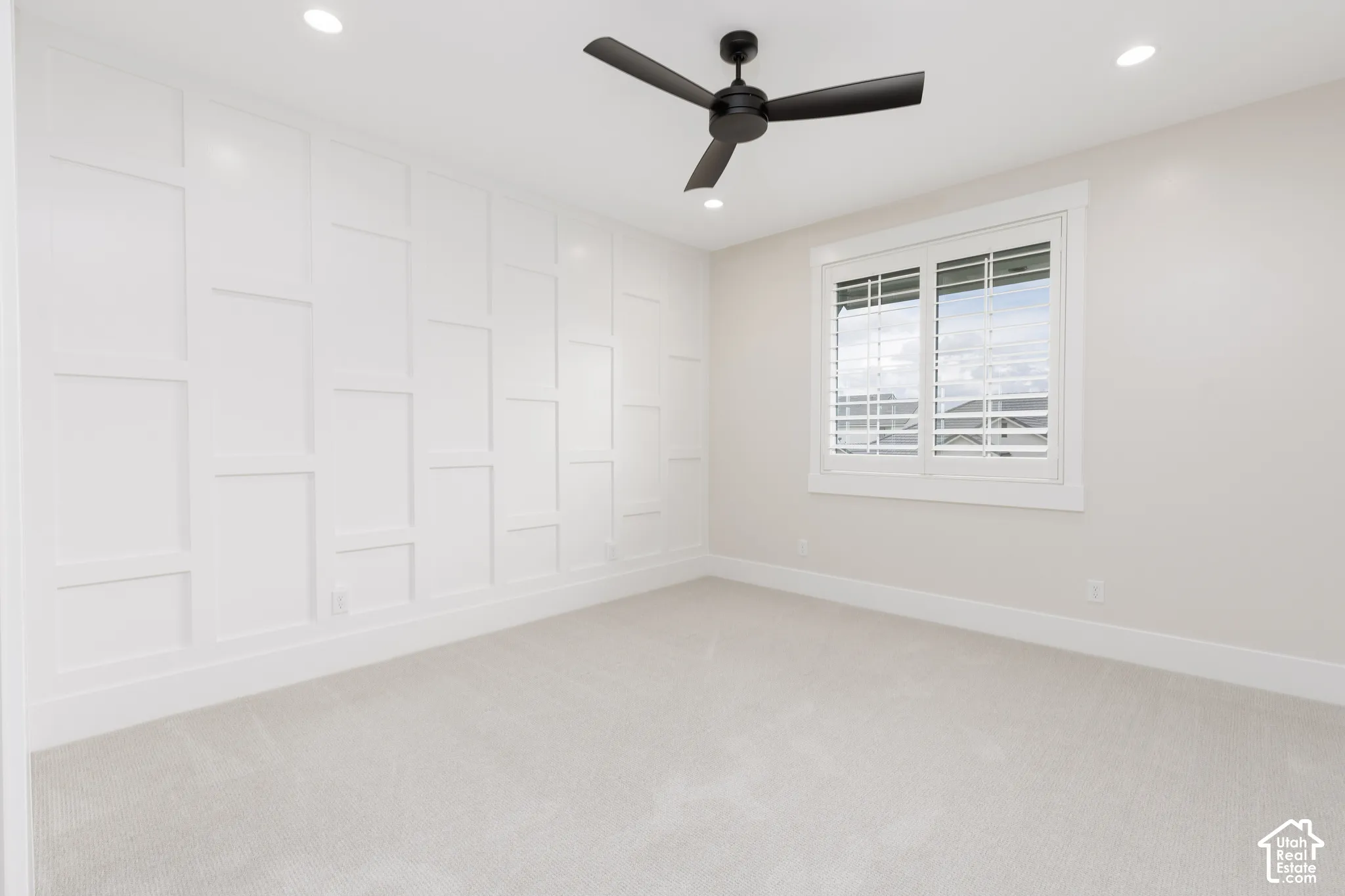 Accent wall with wainscoting detail, matte black ceiling fan, recessed lighting, and plantation shutters