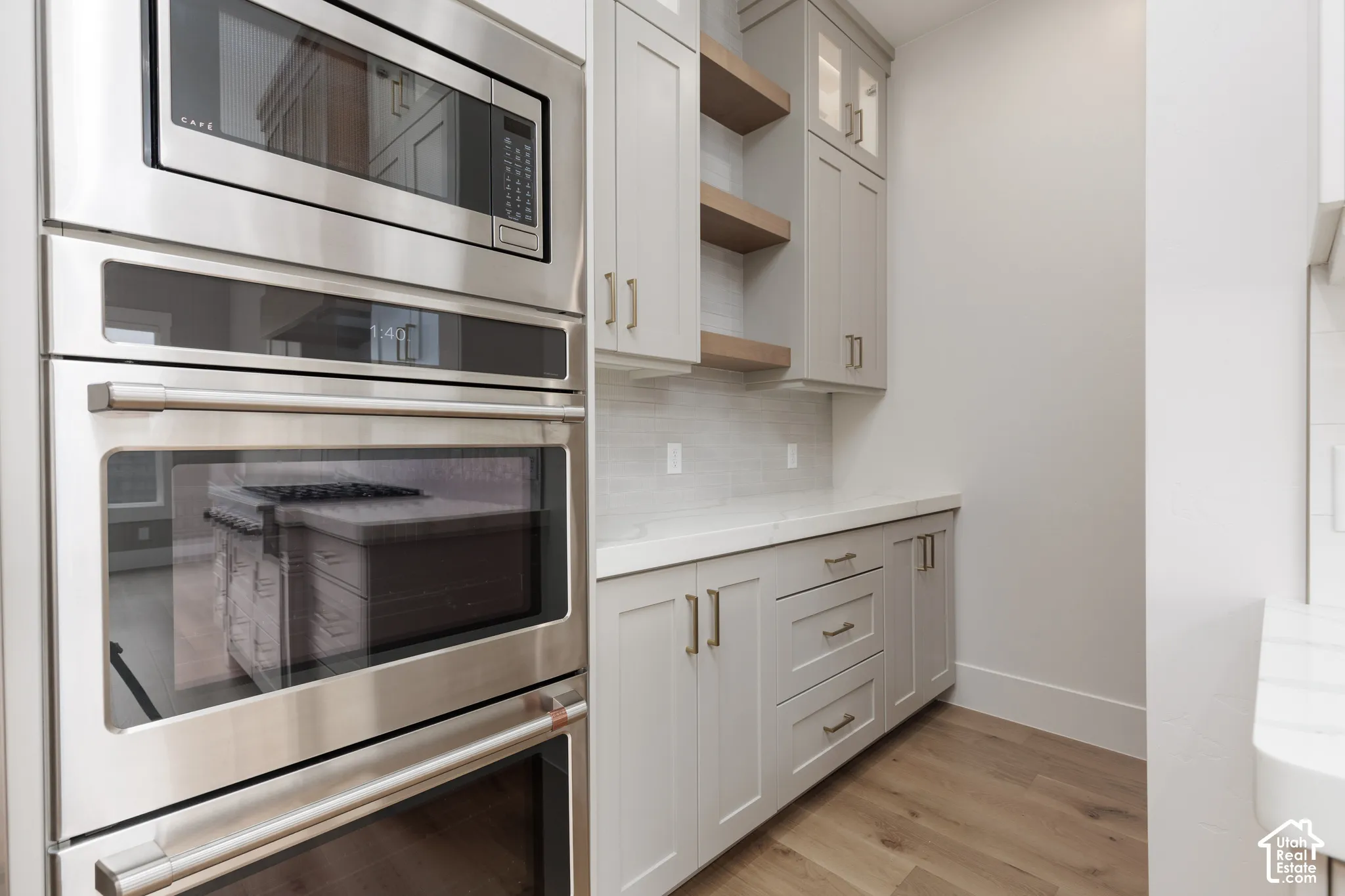 Stainless steel double wall ovens, built-in cabinetry with shaker-style doors, stone-finish countertops, open floating shelving, and wood-finish flooring