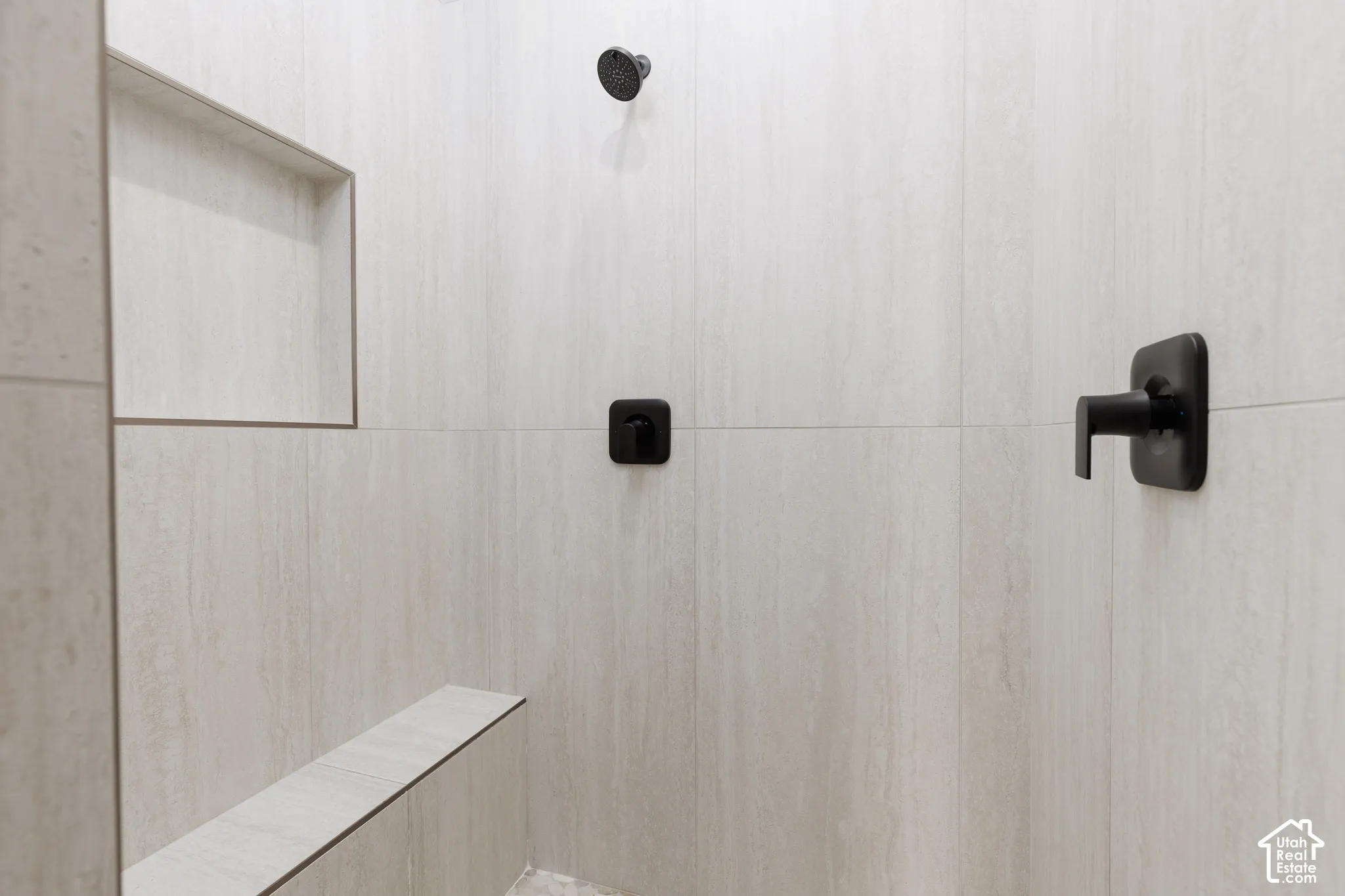 Walk-in shower featuring light-toned large-format tile, matte black fixtures, an integrated wall niche, and a built-in tiled bench