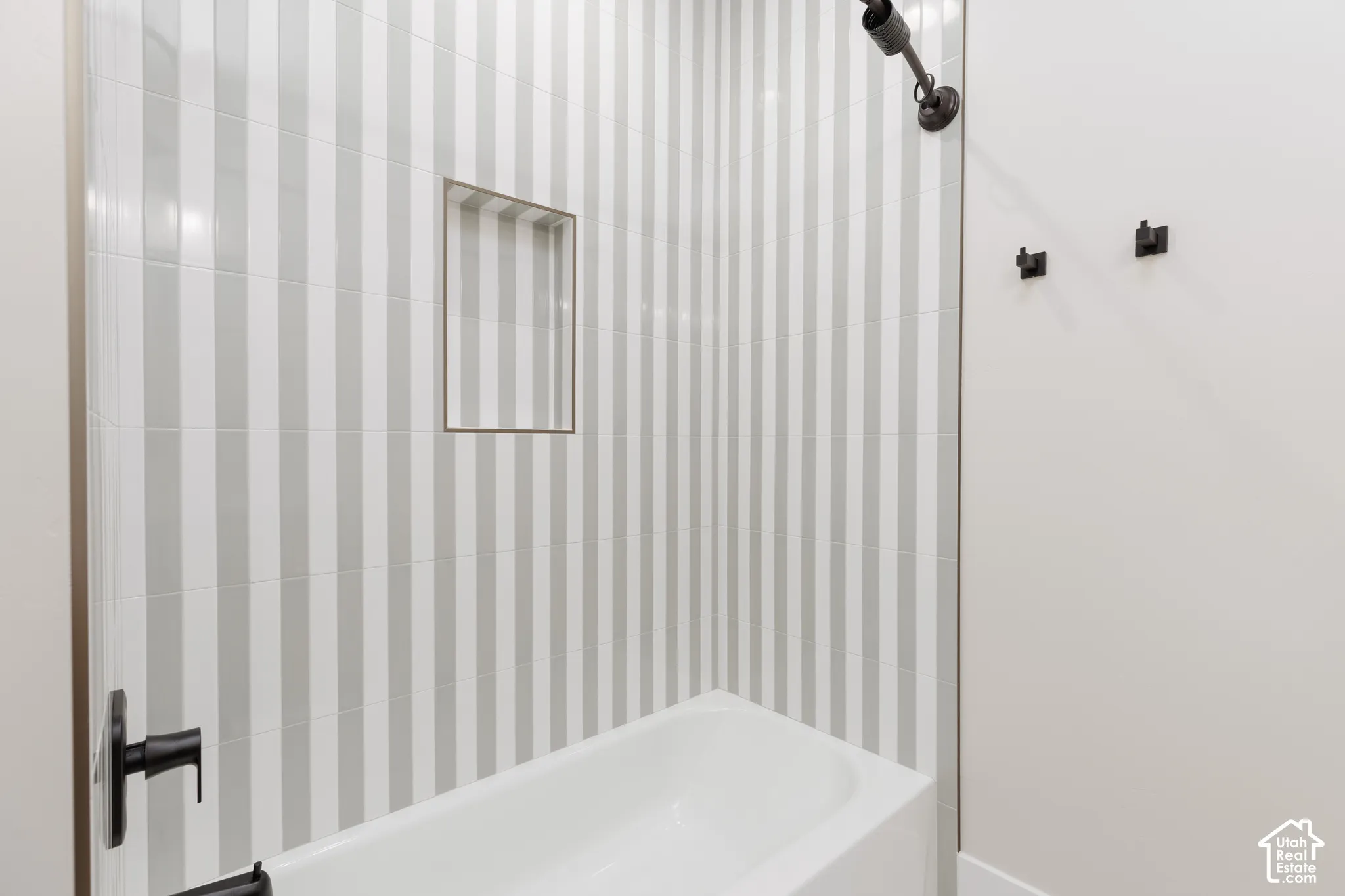 Shower enclosure featuring vertical striped wall tile, built-in recessed wall niche, matte black fixtures, and a white bathtub
