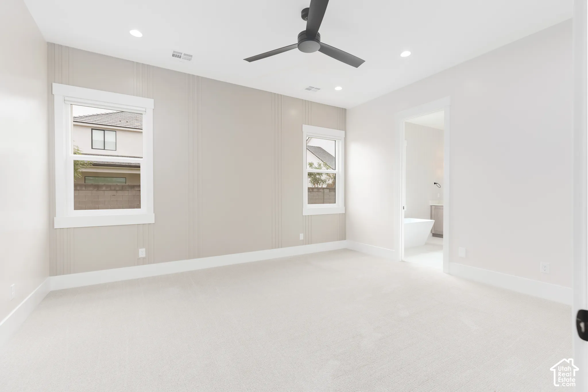 Neutral-toned room featuring a vertical panel accent wall, recessed lighting, carpeted flooring, and a matte black ceiling fan